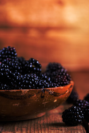 Fresh ripe blackberry in rustic bowl, wooden background