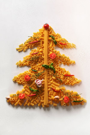 Alternative creative Christmas tree of dry different shape Italian pasta with tomatoes and basil isolated on white background. Xmas vertical greeting card. View from above. Food holiday concept.の写真素材