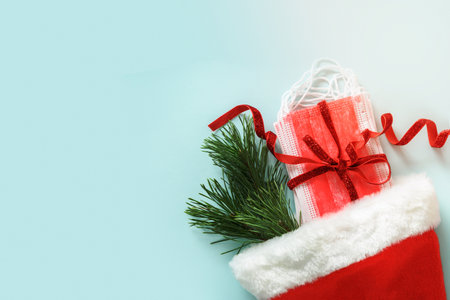 Christmas Santa hat with protective face mask and evergreen pine branches on blue background....