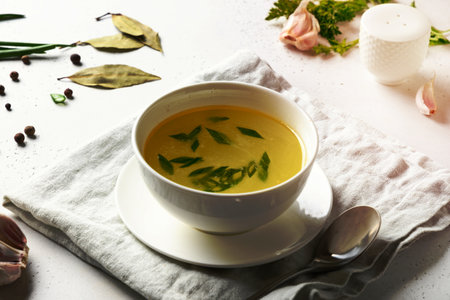 Chicken broth with spices, greens, garlec, parsley, onion in white bowl on white table. Copy space. Close up.の写真素材