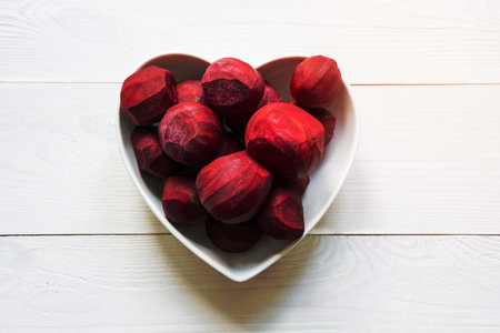 Fresh beet tubers peeled in heart shape plate on white wooden board. View from above. Concept...