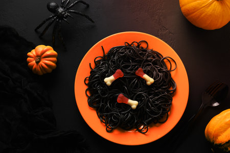 Halloween funny Italian black pasta squid ink decorated horror eyes in orange plate on black background. Horror food for festive party. View from above.の写真素材