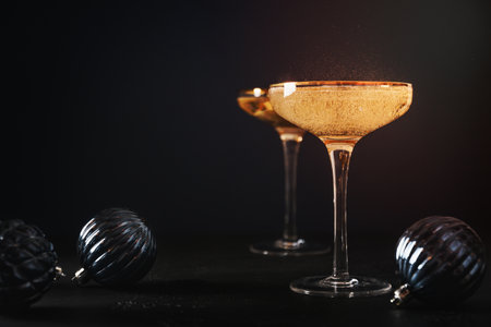 Festive New Year champagne in wine glasses decorated Christmas blue baubles on black background. Close up. Holiday greeting card with copy space.の写真素材