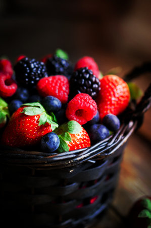 mix of fresh berries in a basket on wooden background