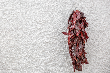 Dry red peppers hung from a hook on a white wall
