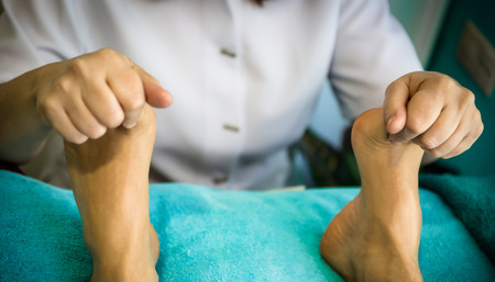 A therapist gives a massage on the feet of a patient lying on a stretcherの写真素材