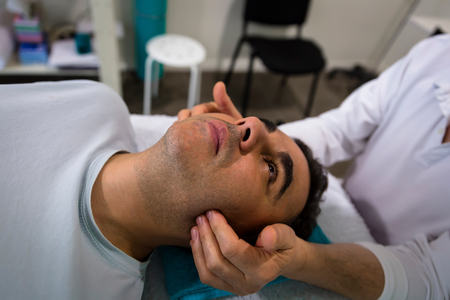 A therapist massages the sides of a relaxed man's faceの写真素材