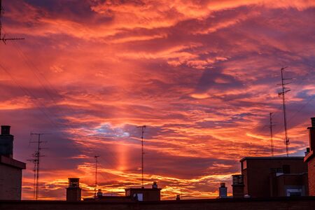 Red and orange sunset in a city, rich in dark clouds, rays of lightの写真素材