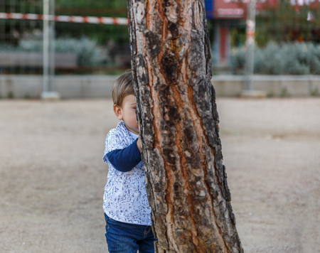 A cute little boy is hiding behind a treeの写真素材
