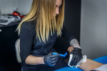 A tattooist girl shaves a part of an arm of her client, in a small studioの写真素材