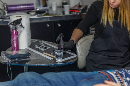 A blonde tattooist sketches a tattoo on the arm of a client in her studio