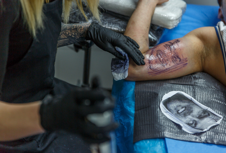 A tattooist girl  is drawing a tattoo on a boy´s arm in her little studioの写真素材