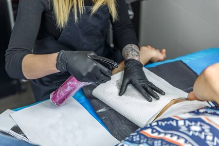 Blonde artist is sketching a tattoo with her tattoo machine on a man's armの写真素材
