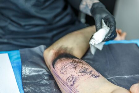 Blonde artist draws with her needle in the arm of a man who is tattooingの写真素材