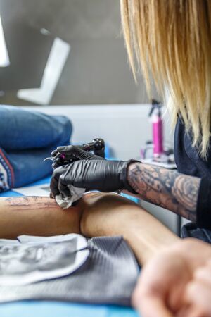 A tattoo artist woman sketches with her needle in the arm of a man who is tattooingの写真素材