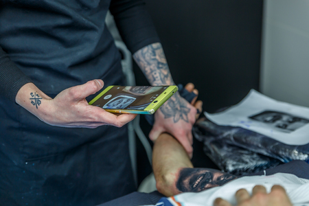 A tattoo artist girl is photographing the tattoo she is doing to her client, in her narrow studioの写真素材