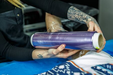 A tattooist blonde girl is covering a special tattoo on the arm of a man, in her little studioの写真素材