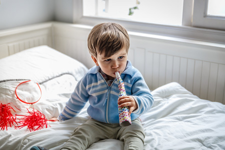 A little boy blows a whistle while on the bed in his bedroomの写真素材