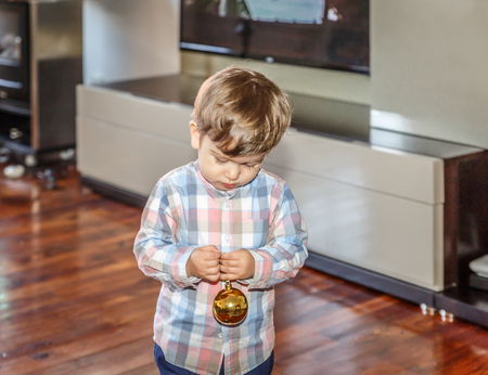 A beautiful blond boy, plays with a decorative Christmas ball in the living room of his homeの写真素材