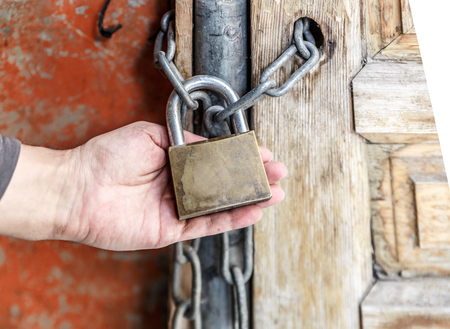 A hand holds a padlock that keeps a wooden door closedの写真素材