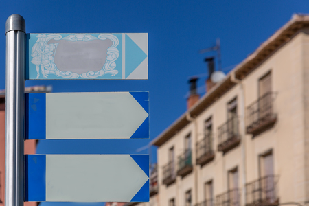 Classic style posters hanging on a metal pole with some buildings in the background, on a sunny dayの写真素材
