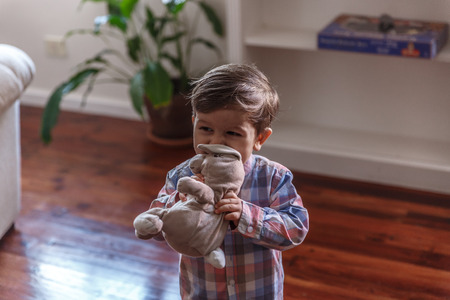 A tender child plays with his bunny doll in the cozy living room of his homeの写真素材