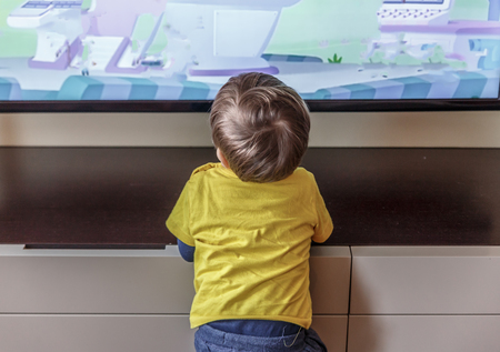 A cute blond boy is watching television very close to it, in the living room of his houseの写真素材