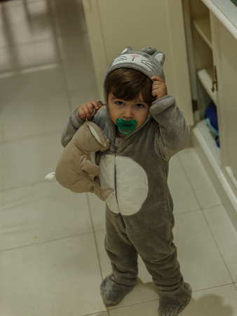 A cute little boy with a very funny pajamas and a pacifier, is playing in the hallway of his house.の写真素材