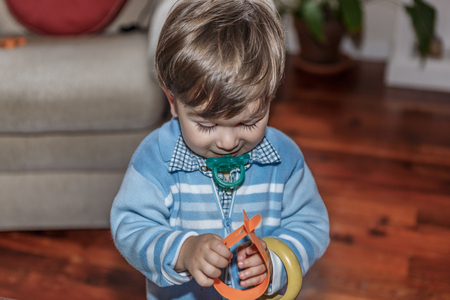 A cute blond child with a pacifier plays with some bracelets in the living room of his houseの写真素材