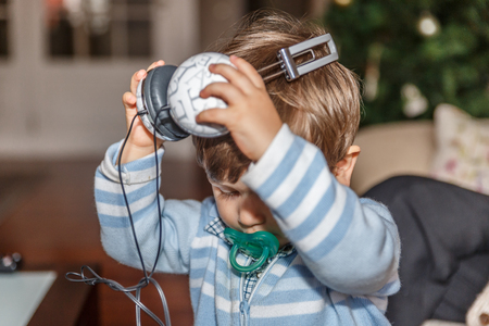 A cute child is ready to listen to music with a large headset while in the living room of his homeの写真素材