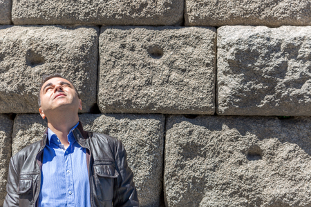 Man with leather jacket and blue shirt looks towards the sun while on the streetの写真素材