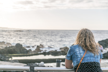 A tourist woman observes the sea while resting on a long railing.の写真素材