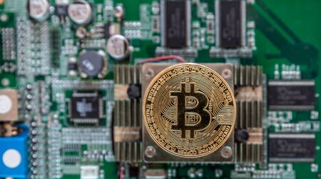 View of a large golden bitcoin placed on a chipset of a graphics card with lots of circuitry and background processorsの写真素材