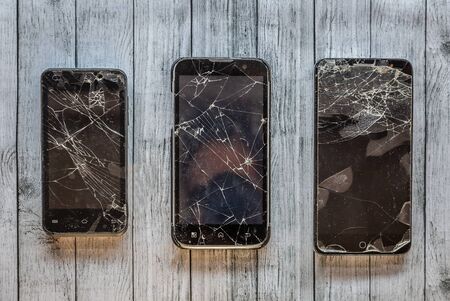 Set of three broken black mobile phones of different sizes, ready to repair your screens, on a light gray surfaceの写真素材