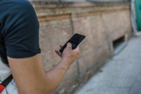 View from behind of a strong arm of man holding a black smartphone while walking down the streetの写真素材