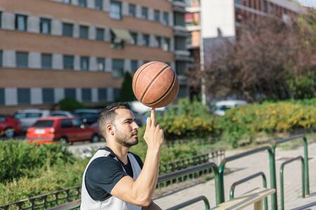 Strong build basketball player spins a basketball over his middle finger of his right hand, on an...