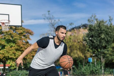 Attractive and strong urban player plays basketball outdoors on a court on a beautiful sunny summer...
