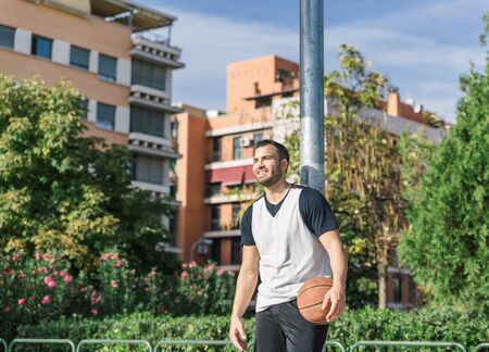 Attractive urban basketball player smiles while leaning on an outdoor metal columnの写真素材