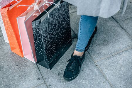 Pink, black, orange and white shopping bags resting on the floor next to the feet of a woman wearing jeansの写真素材