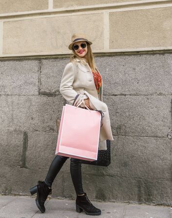 Attractive woman with a lot of style carries a pink shopping bag while walking through a city street on a cold dayの写真素材