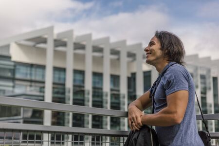 Smiling and happy Caucasian man leaning on a metal railing outdoors in a city on a spring day