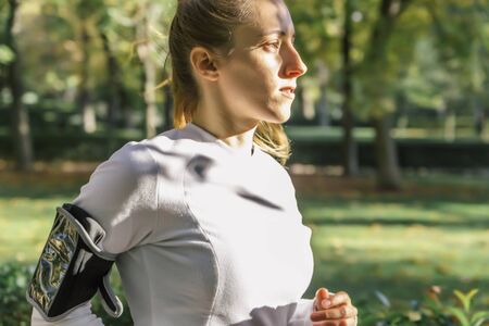 Portrait of a blonde young woman running through a park with lots of nature in the background