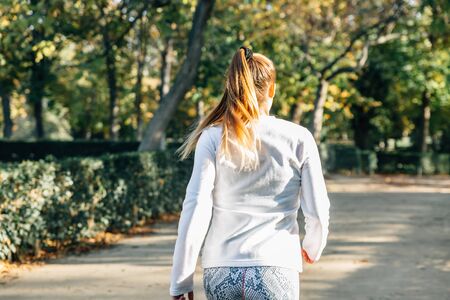 Back view of a woman runner exercising in a park with a lot of green in the background in summerの写真素材