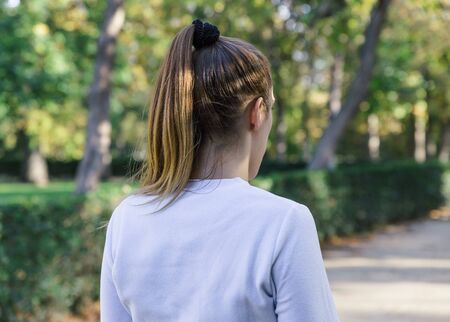 Back view of a blonde female runner in a white t-shirt in a park with lots of nature