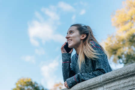 Happy Caucasian young woman talking in a park with her mobile phone on a sunny day.の写真素材