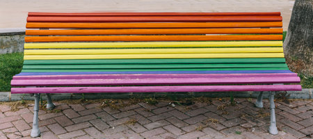 Bench in the middle of a park with the colors of the gay flag on a nice dayの写真素材
