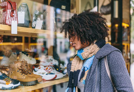Attractive stylish afro hair girl looks at a shop window on a shopping dayの写真素材