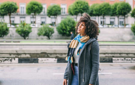 Dark skinned woman with afro hair on the street of a city on a cold day