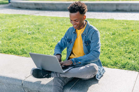 Happy man writes on his laptop in a nice park sitting near a green areaの写真素材