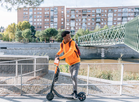 Happy young man in casual wear prepares with his electric scooter next to a bridge in a cityの写真素材